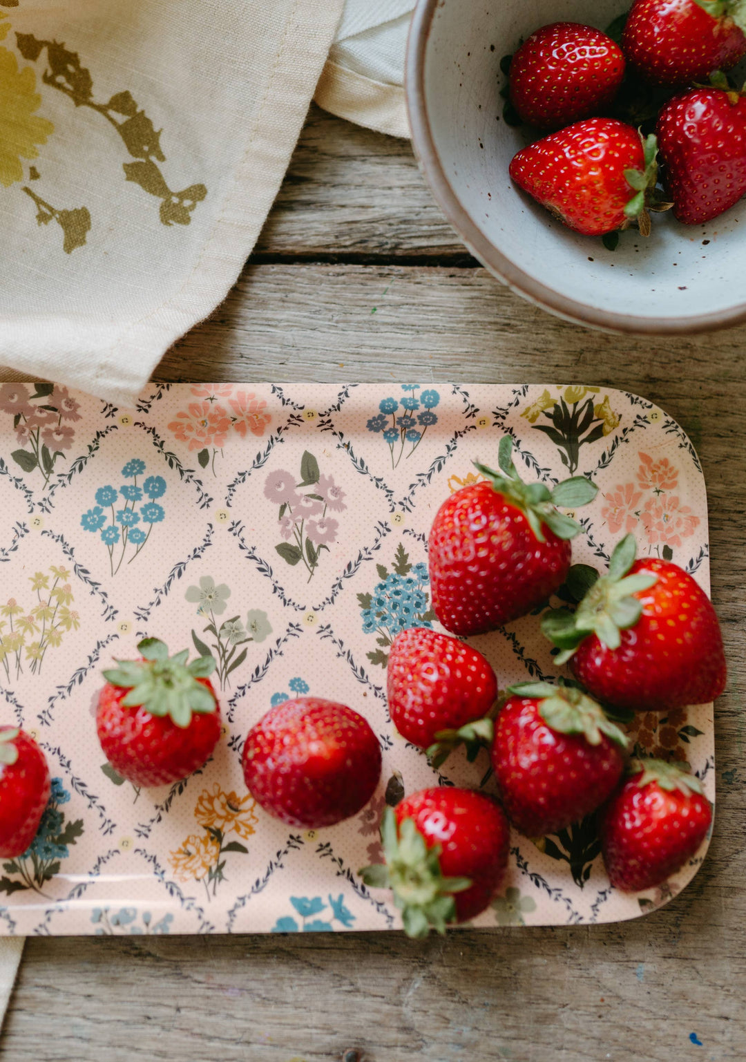 Strawberries on a floral-patterned tray with a bowl of strawberries in the background.