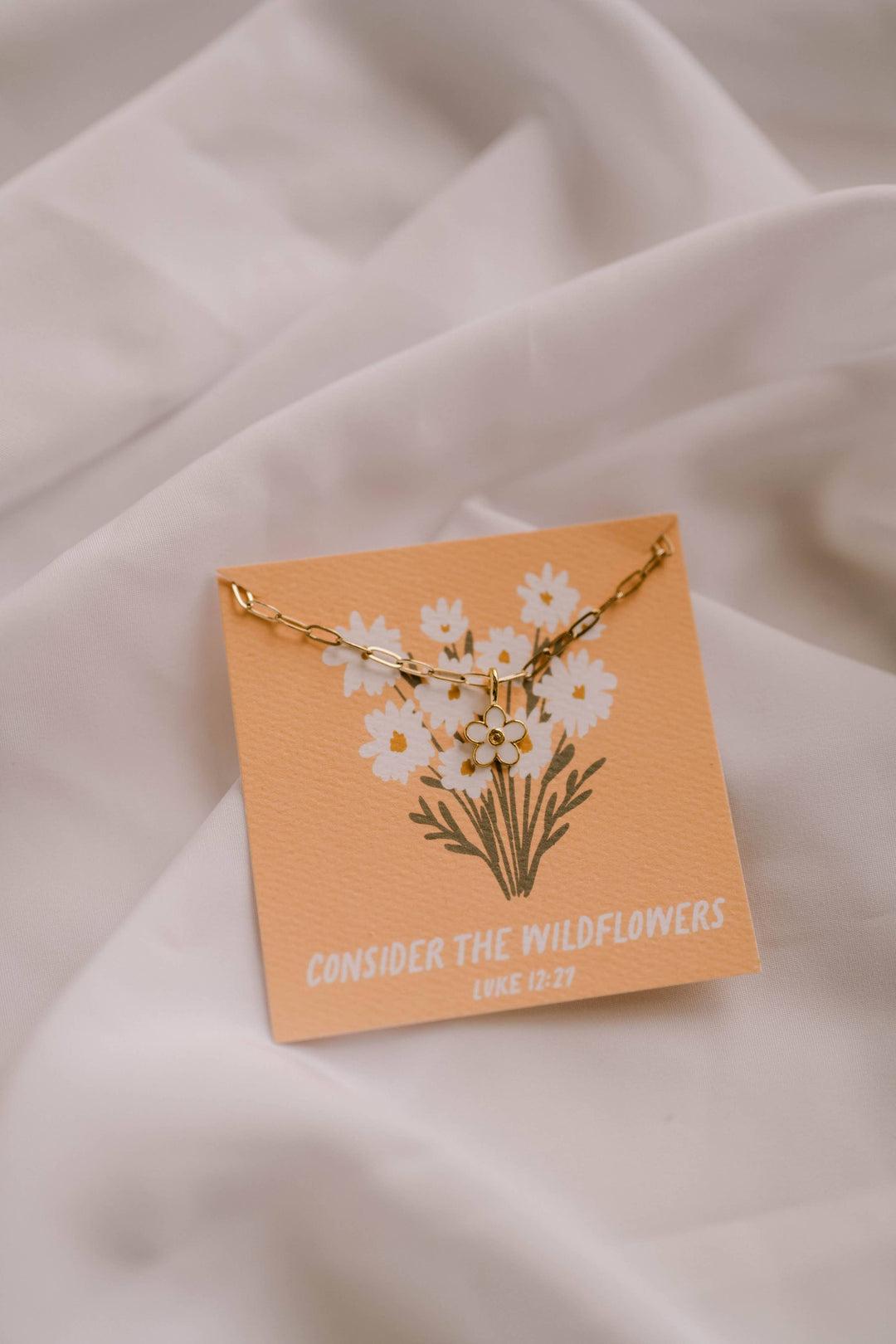 Necklace with floral design on a matching card against a soft fabric background