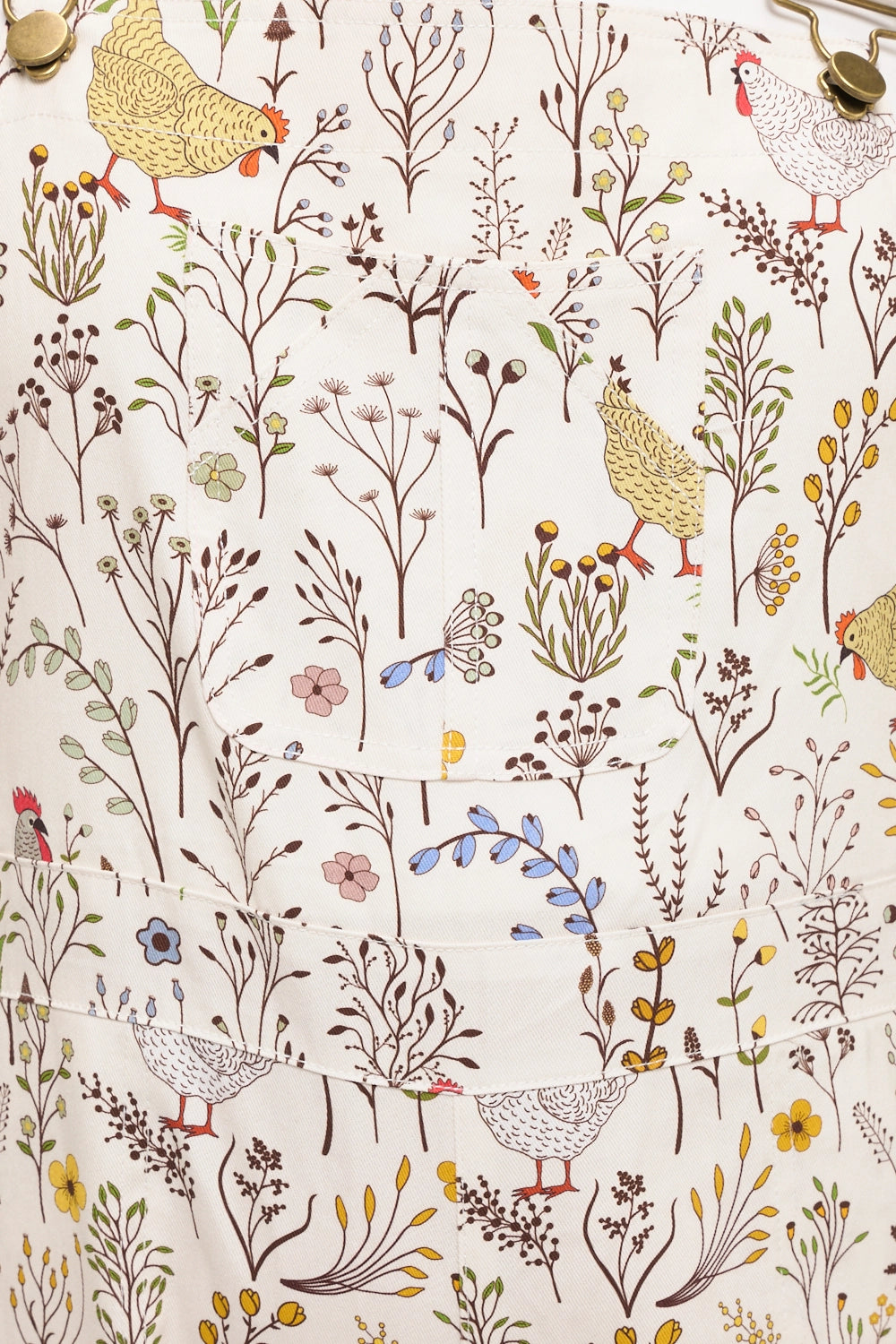 Close up of overalls print with chickens, roosters and botanicals