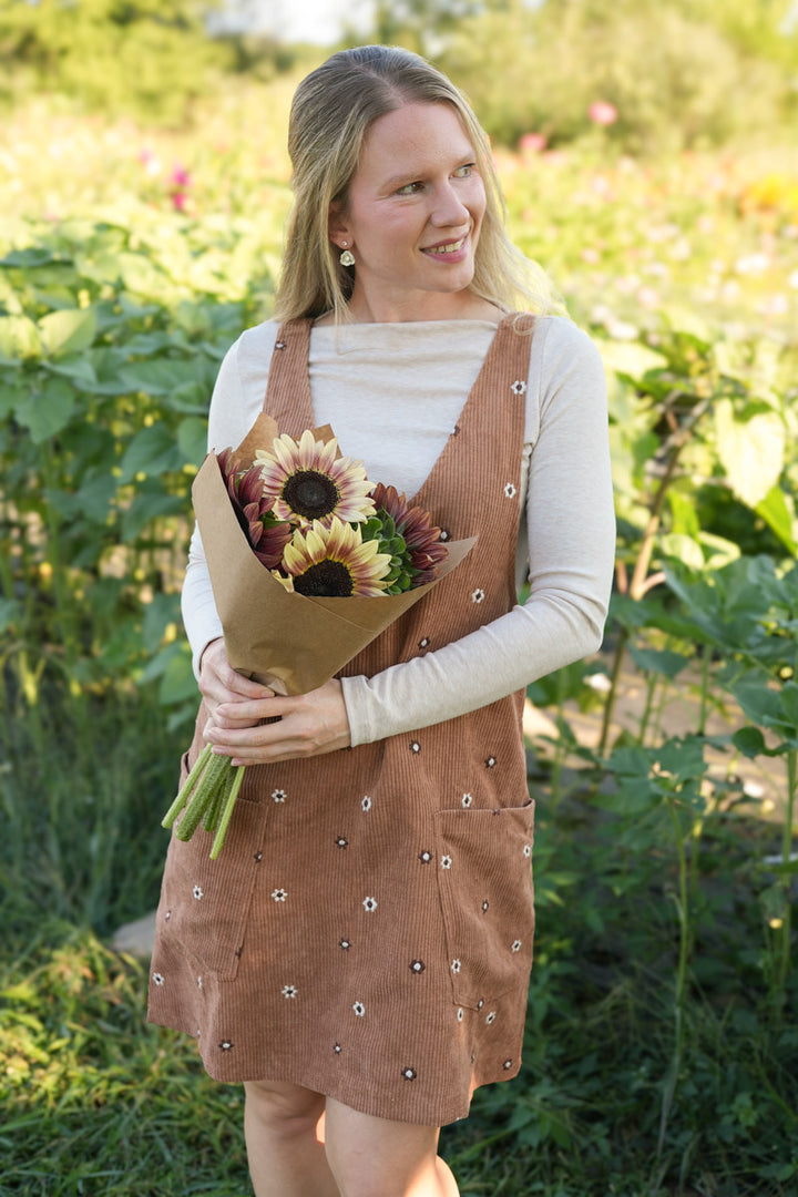 Woman wearing a brown floral corduroy dress holding a bouquet of sunflowers in an outdoor setting