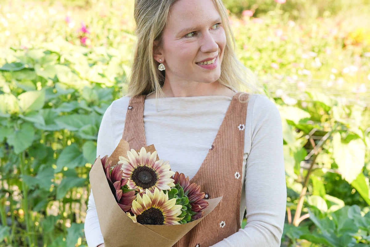 Woman wearing floral overalls holding a bouquet of sunflowers in a field