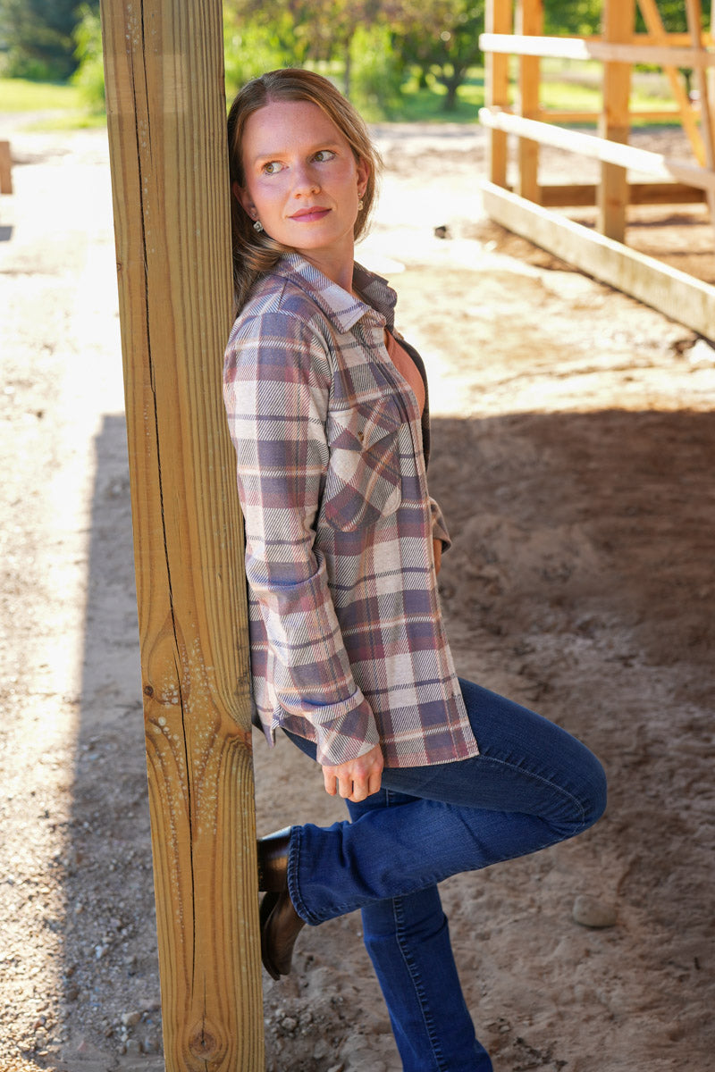 Woman in plaid shirt and jeans standing next to a wooden post outdoors.