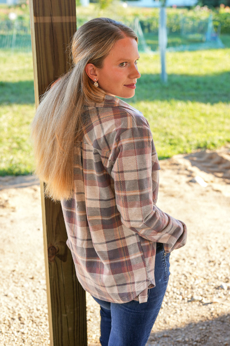 Woman wearing a plaid shirt standing outdoors near a wooden structure.