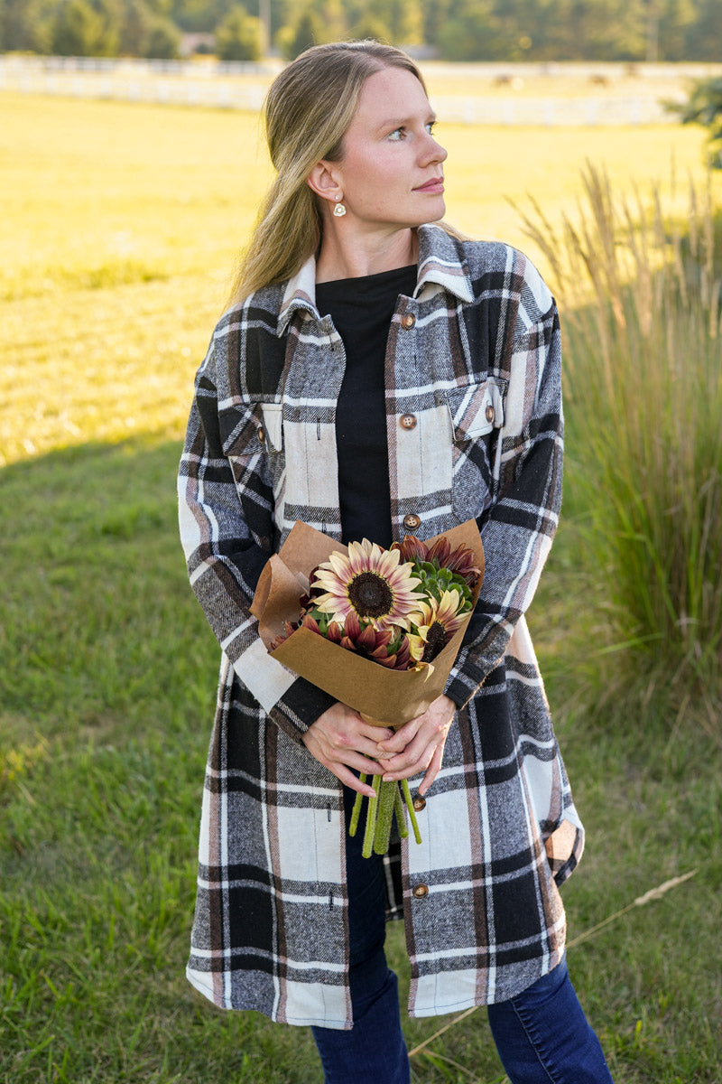 Woman in a long plaid coat holding a bouquet of sunflowers in a field