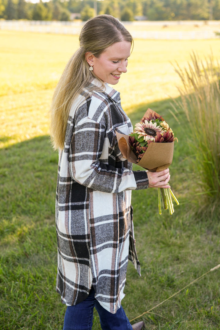 Woman in a plaid coat holding a bouquet of sunflowers in a field