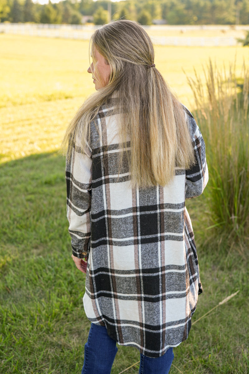 Woman wearing a long plaid shirt in white, black and brown standing in a field