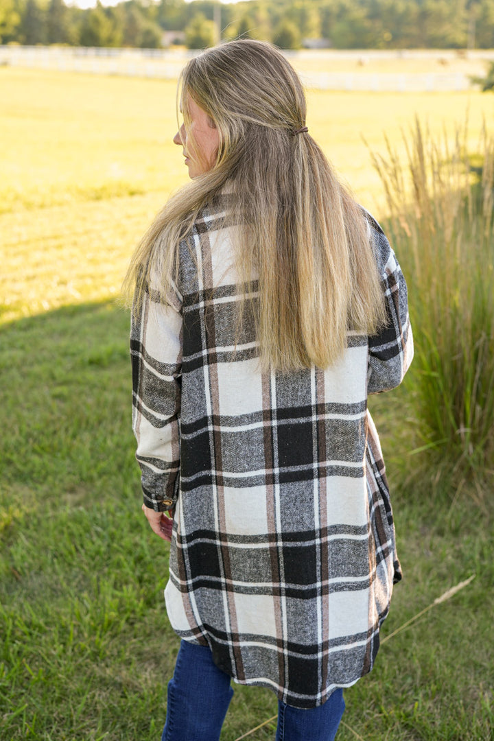 Woman wearing a long plaid shirt in white, black and brown standing in a field