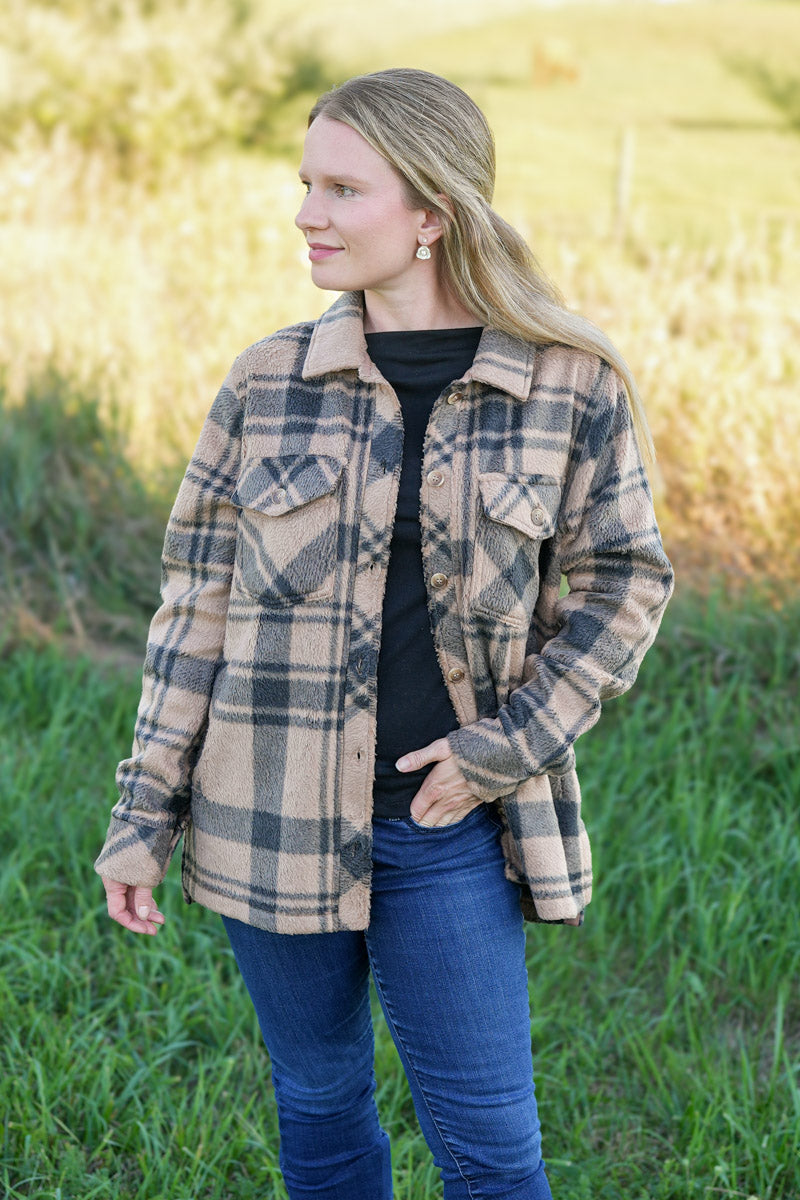 Woman wearing a black and tan plaid fleece jacket in a natural setting