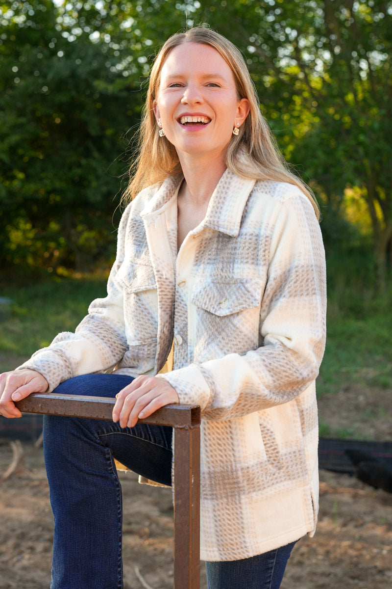 Woman wearing a plaid fleece jacket sitting outdoors with trees in the background