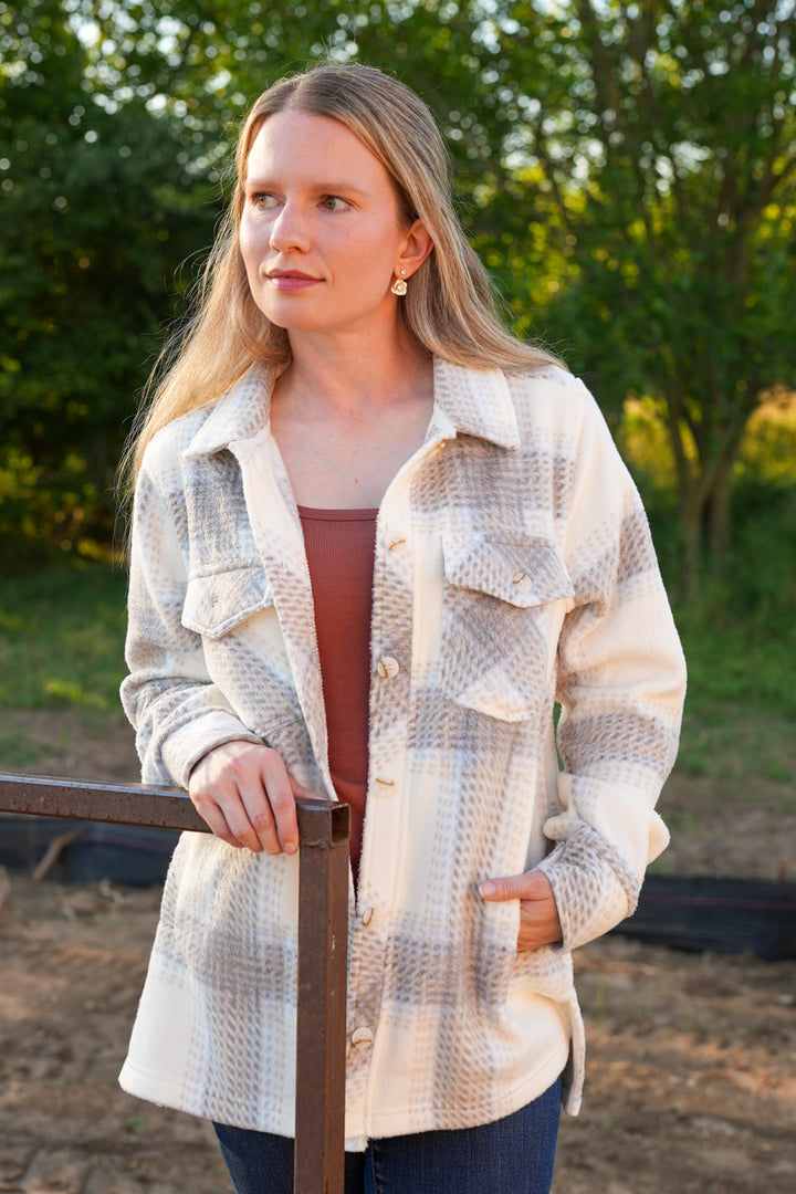 Woman wearing a plaid jacket outdoors with trees in the background