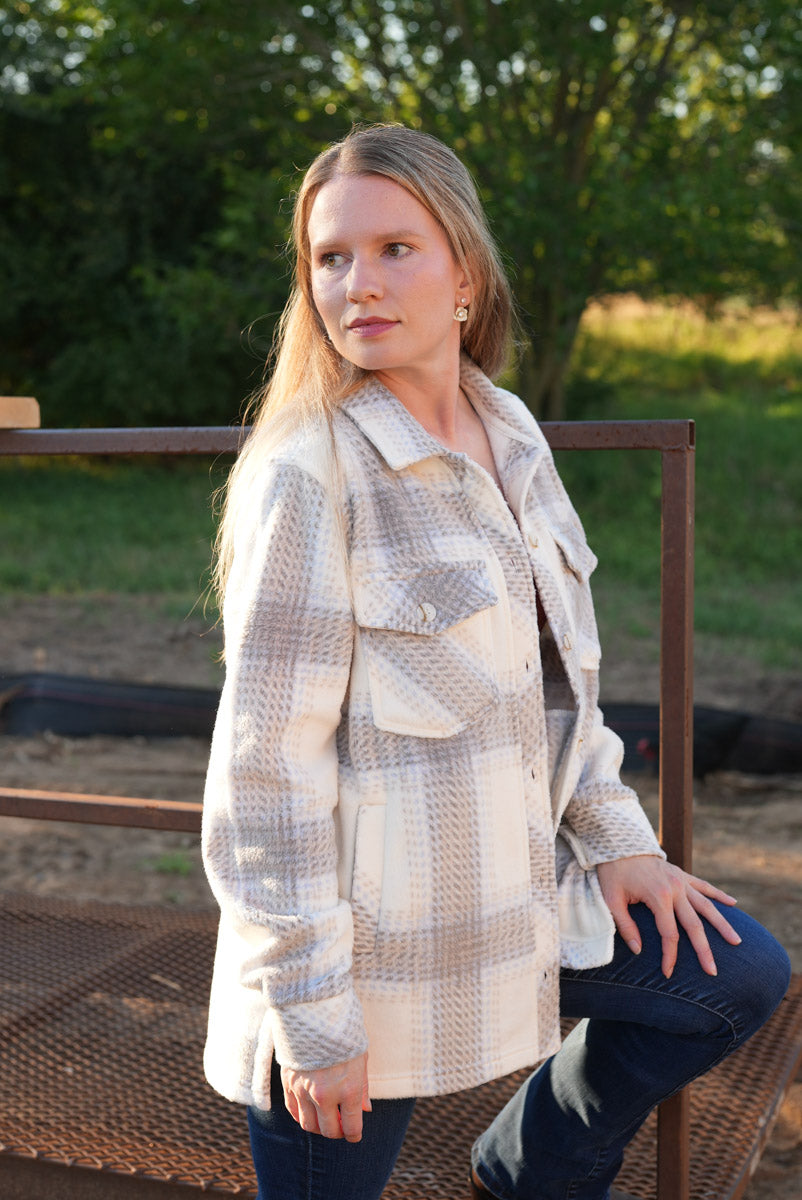 Woman wearing a plaid coat sitting outdoors with greenery in the background