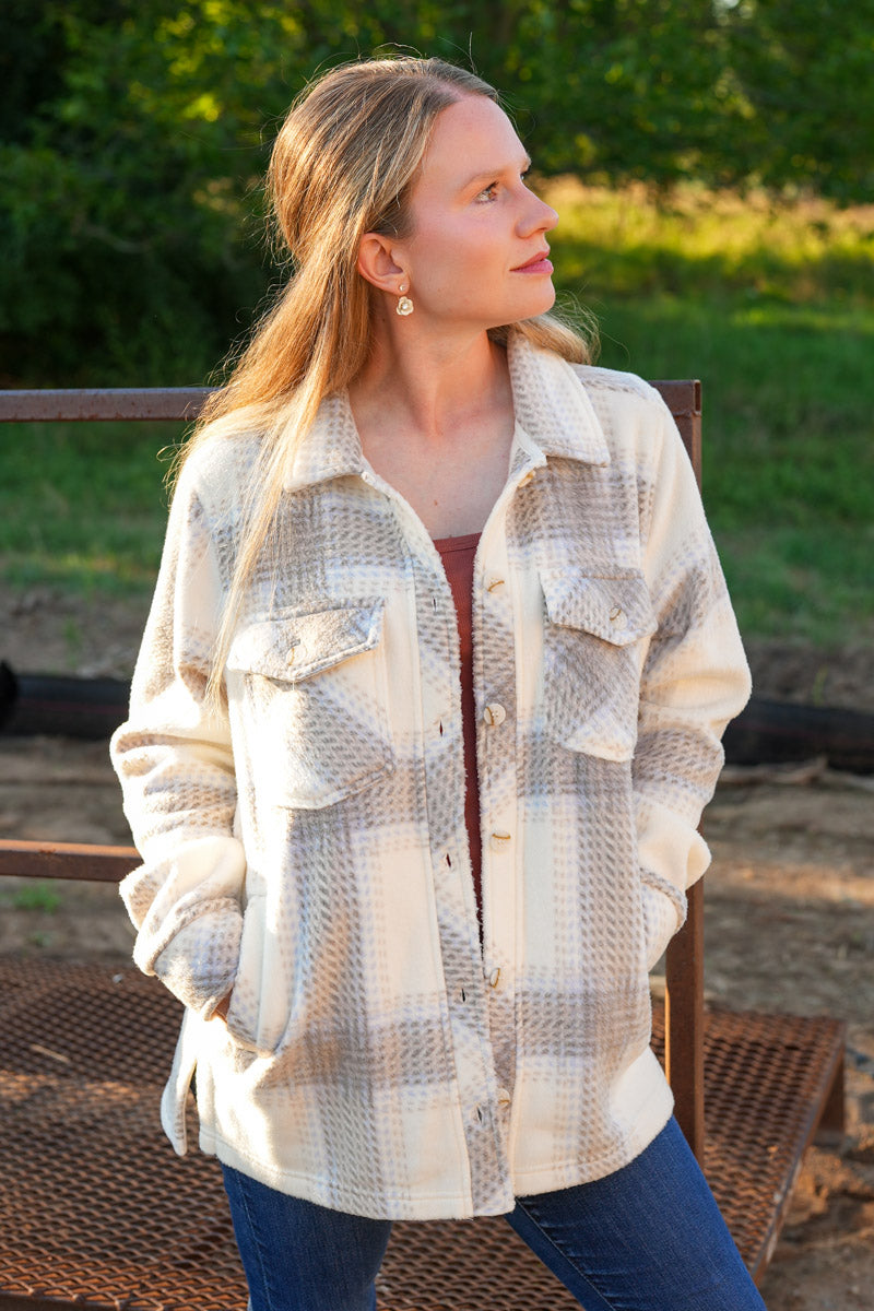Woman wearing a plaid fleece jacket sitting outdoors with greenery in the background