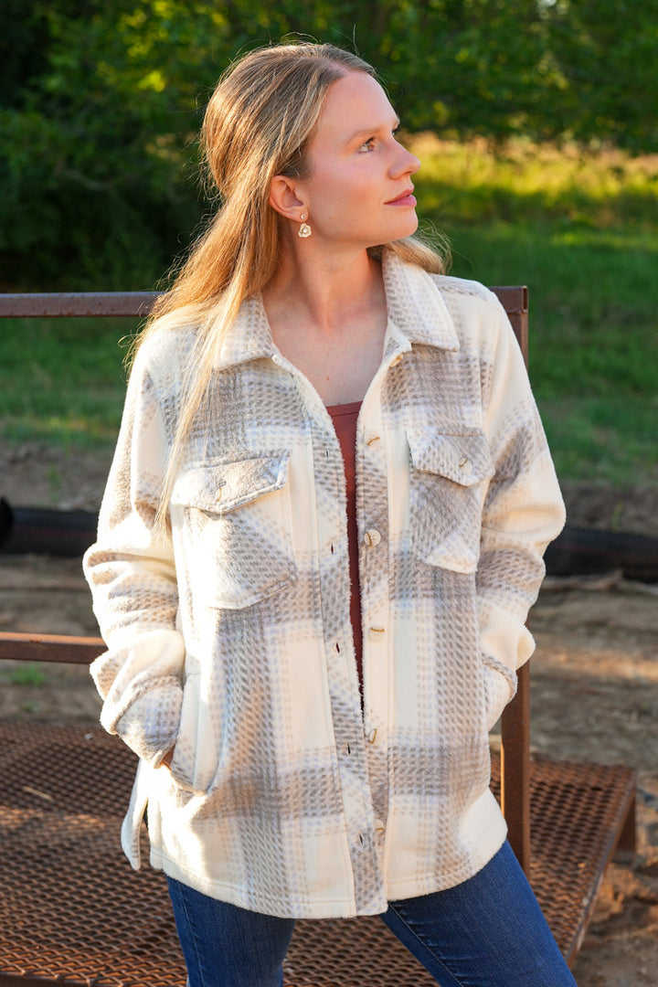 Woman wearing a plaid fleece jacket sitting outdoors with greenery in the background