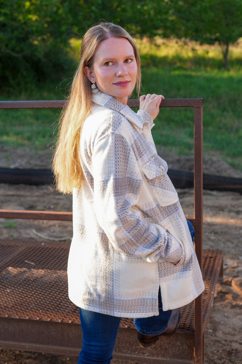 Woman wearing a plaid fleece coat standing outdoors with greenery in the background