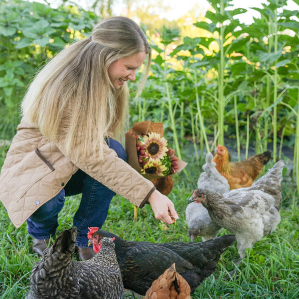 Woman wearing barn coat feeding chickens in a garden setting