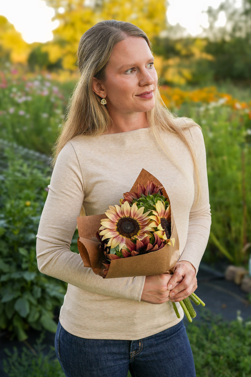 Woman wearing a taupe long sleeve boat neck top holding a bouquet of sunflowers