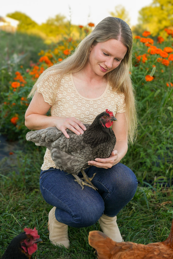Woman holding a chicken in a garden with flowers and other chickens in the background
