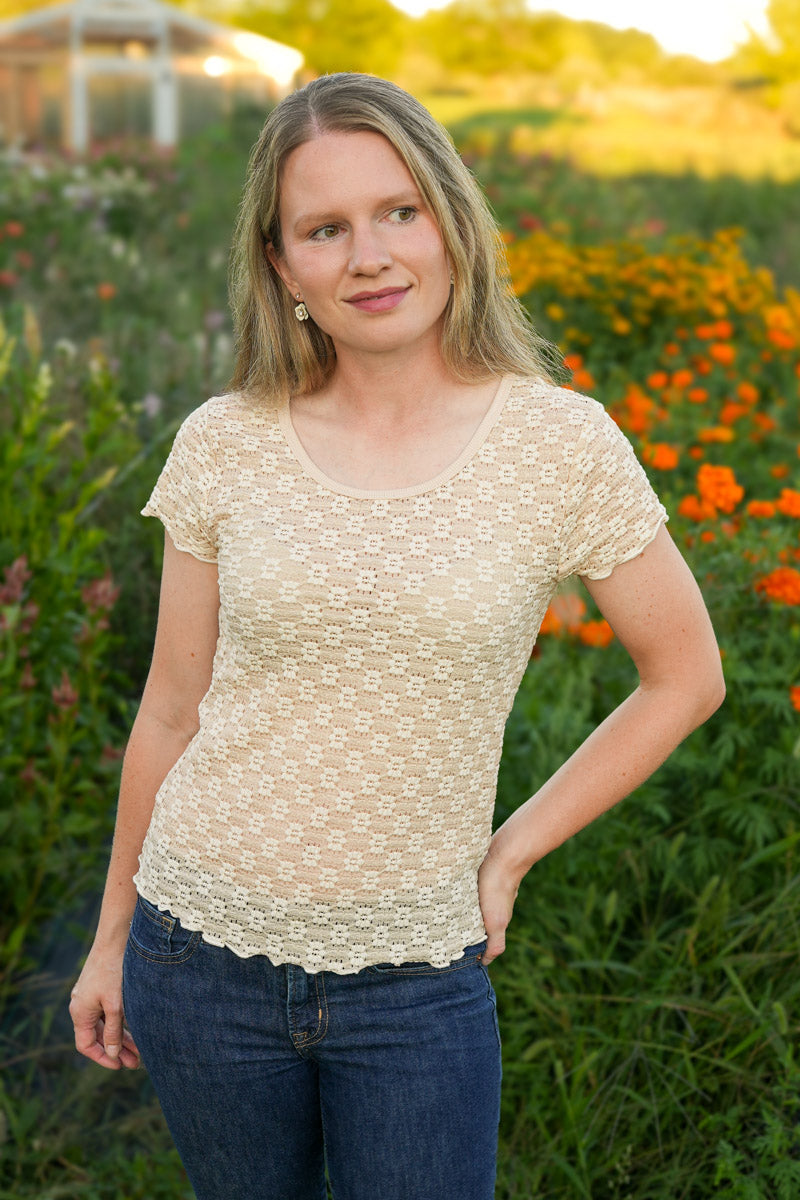Woman wearing a beige top and blue jeans standing in a field with flowers