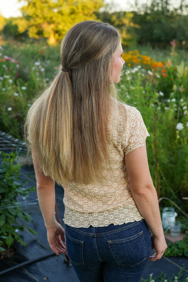 Woman wearing a beige floral lace T-shirt standing in a garden