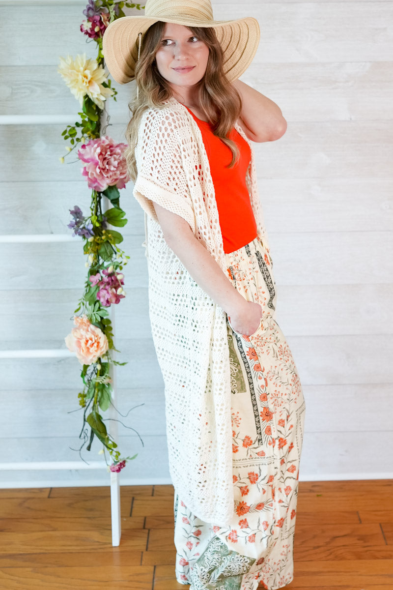 Woman in a red top and white crochet cover-up standing next to floral decorations indoors.