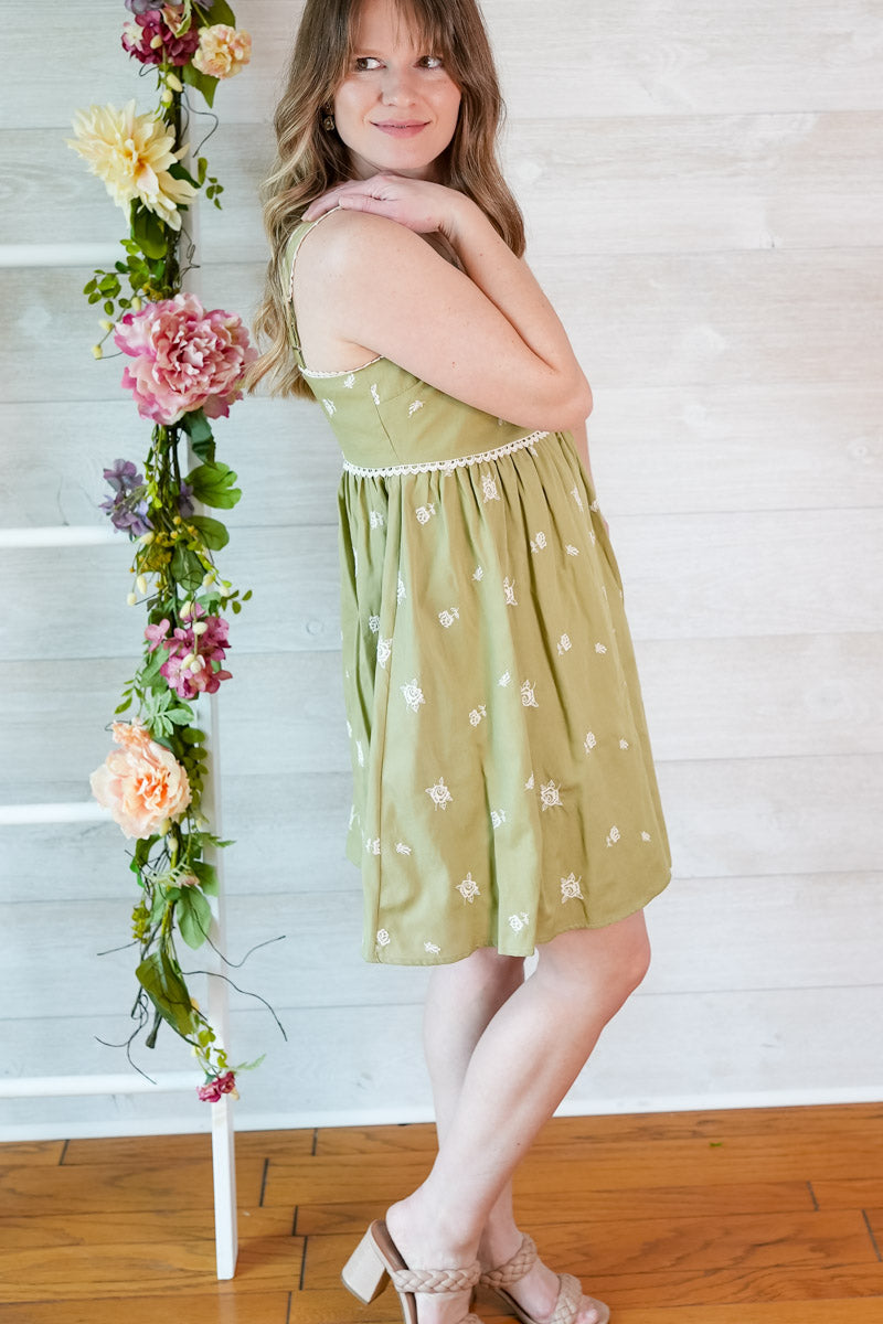 Woman in a green dress standing next to a floral arrangement against a white wooden wall.