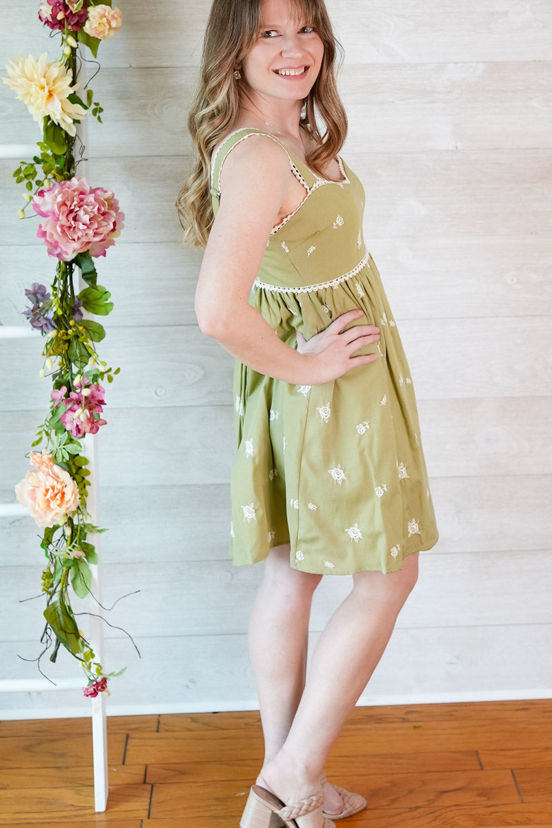 Woman in a green dress standing next to a floral arrangement against a white wooden wall.