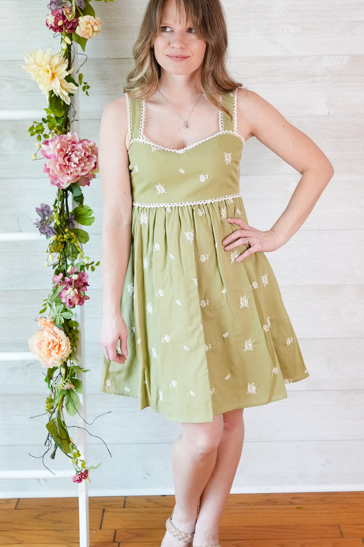 Woman wearing a green dress with floral decorations on a wooden floor.