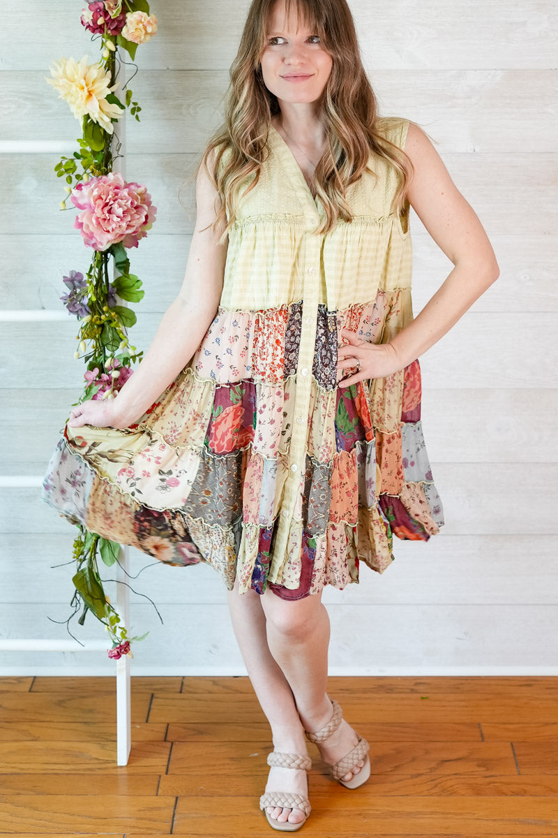 Woman wearing a colorful patchwork dress with floral decorations on a wooden floor.