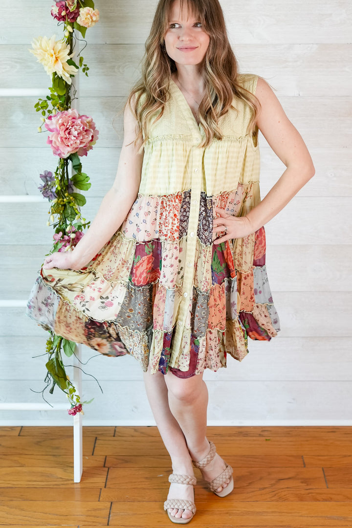 Woman wearing a colorful patchwork dress with floral decorations on a wooden floor.