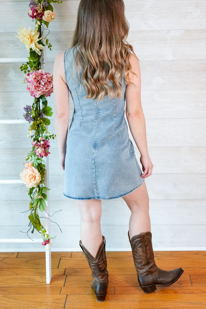Woman wearing cowboy boots and a light wash denim mini dress with ribbon detailing and zip up back