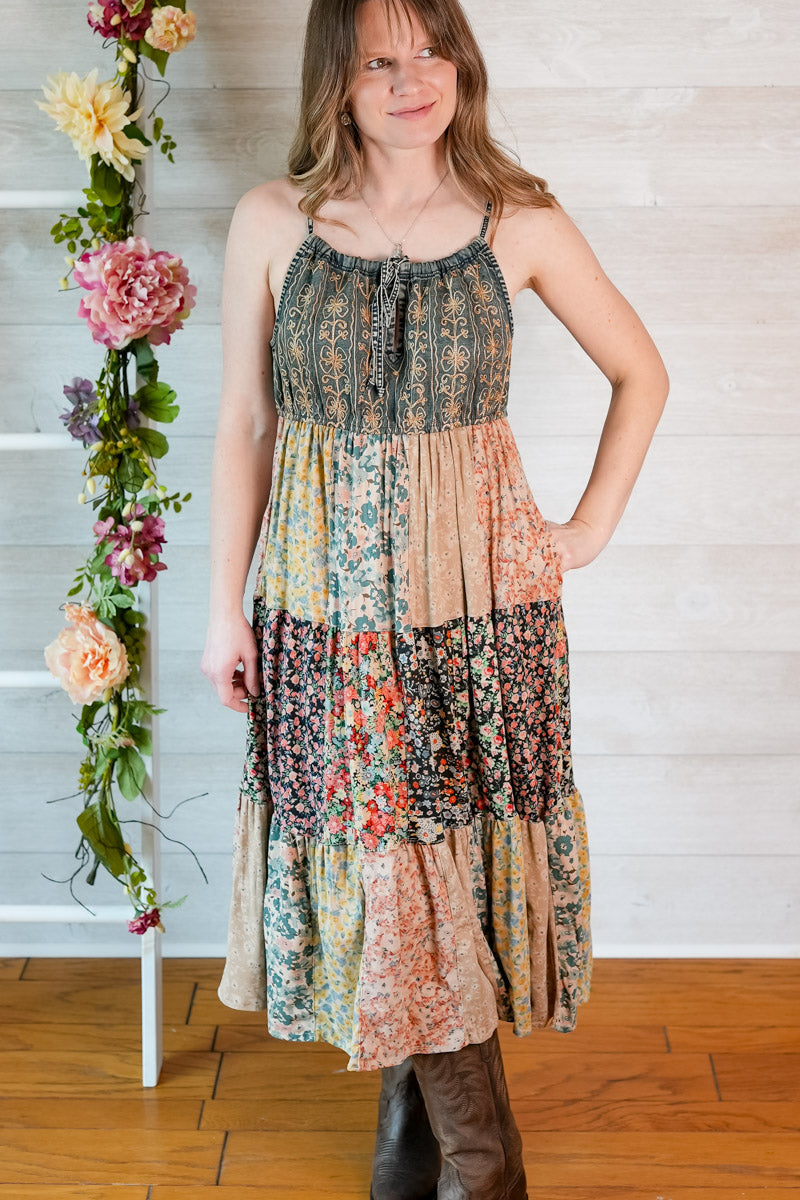 Woman wearing a floral tiered dress standing next to a floral arrangement indoors.