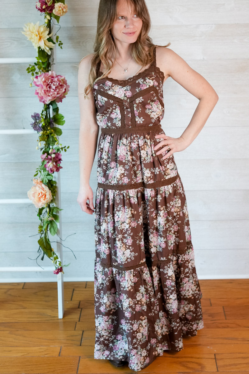 Woman wearing a western-inspired floral maxi dress standing next to a floral arrangement indoors.