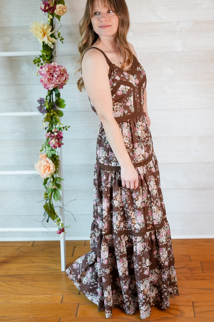Woman wearing a brown floral print maxi dress standing next to a floral arrangement indoors.