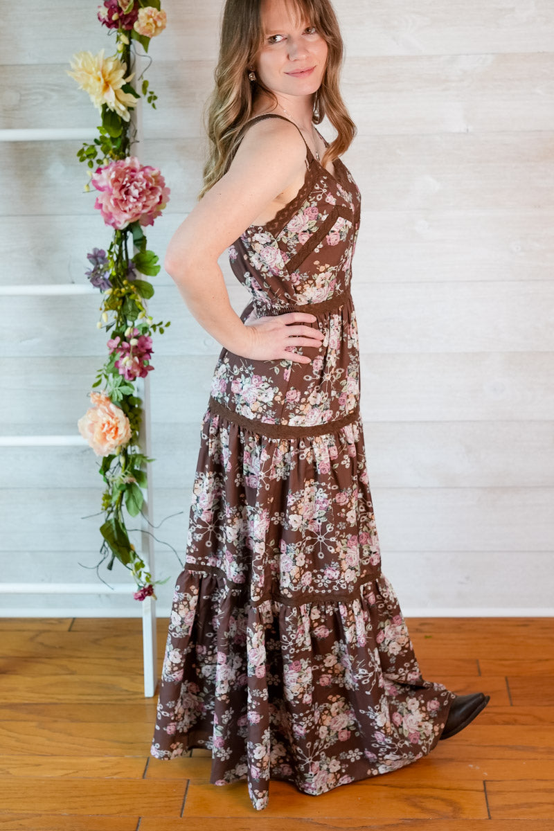 Woman wearing a brown western inspired floral maxi dress standing next to a floral arrangement indoors.