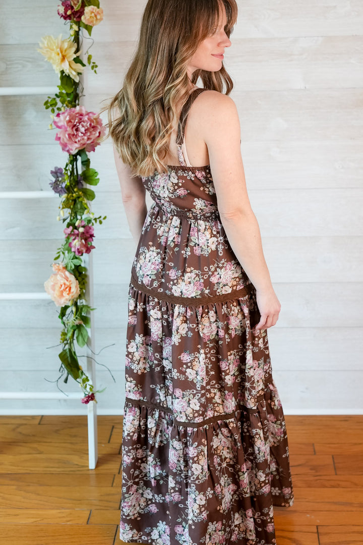 Woman wearing a brown floral western-inspired maxi dress standing next to a floral arrangement indoors.