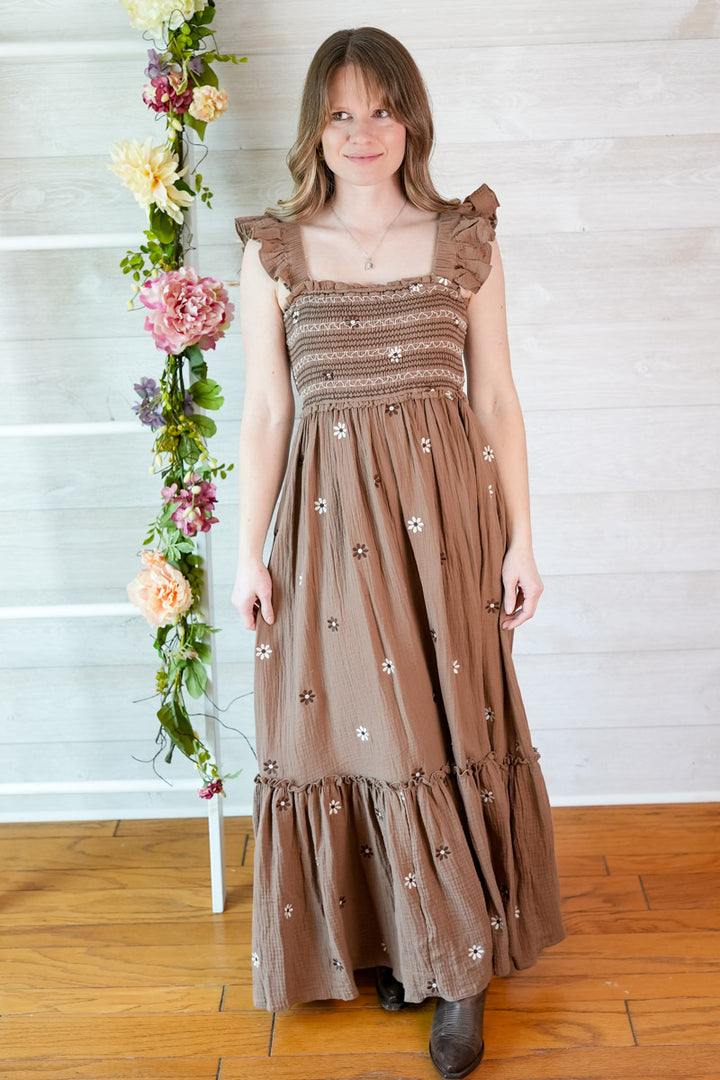 Woman wearing a brown floral dress standing next to a floral arrangement indoors.