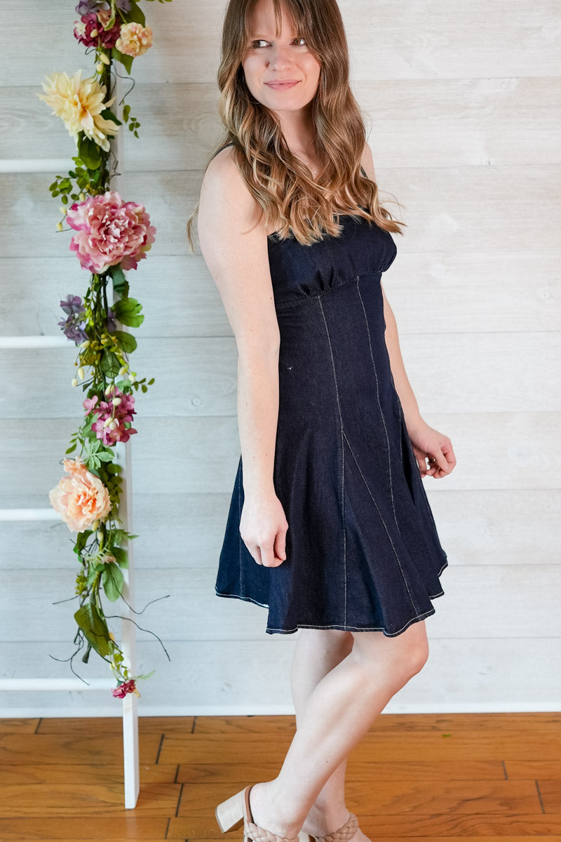 Woman in a navy blue dress standing next to a floral arrangement against a white wall.
