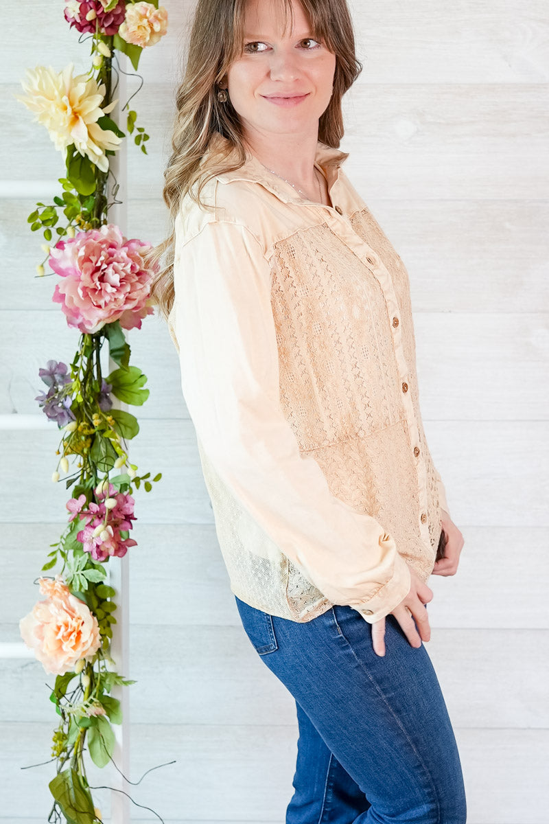 Woman wearing a beige blouse and blue jeans standing next to a floral arrangement against a white wooden background