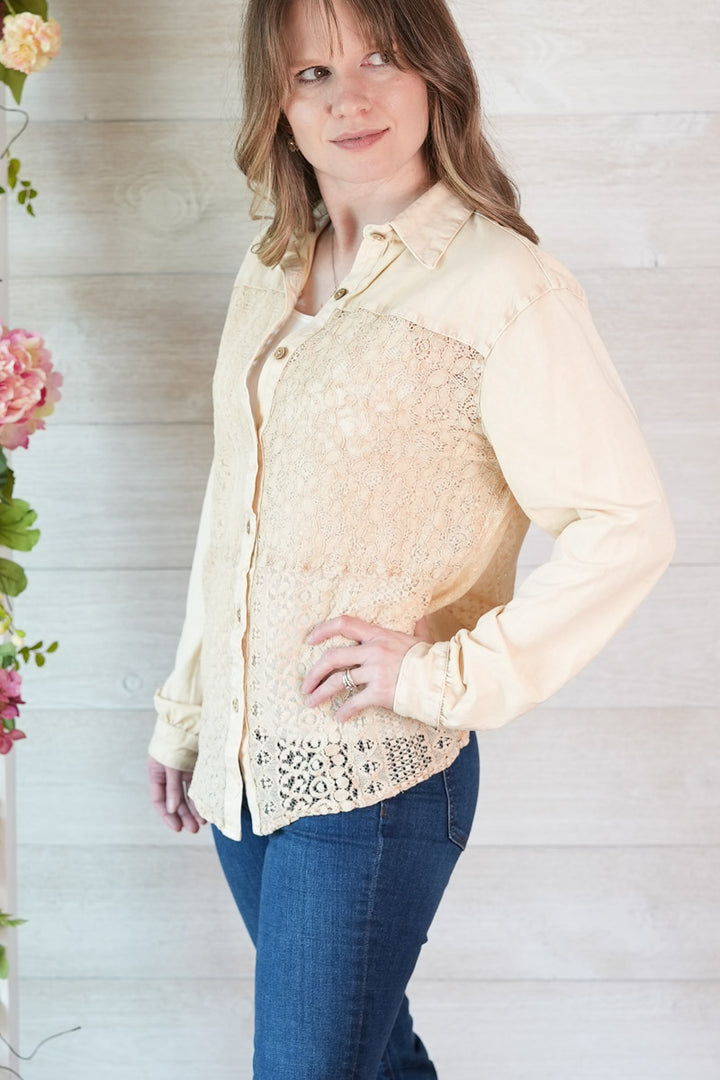 Woman wearing a cream lace blouse and blue jeans against a light wooden background