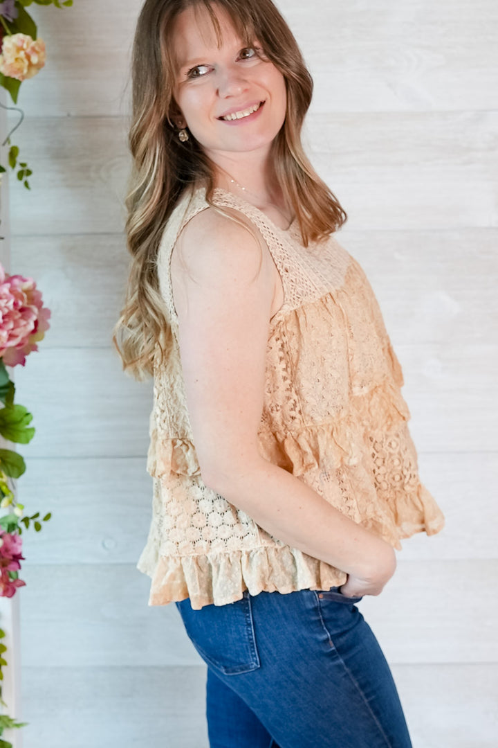 Woman wearing a beige tiered lace tank top and blue jeans against a light wooden background