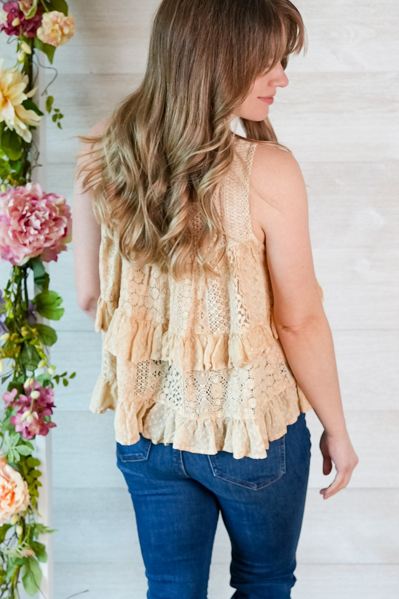 Woman wearing a beige lace tiered tank top and blue jeans with floral decorations on the side.
