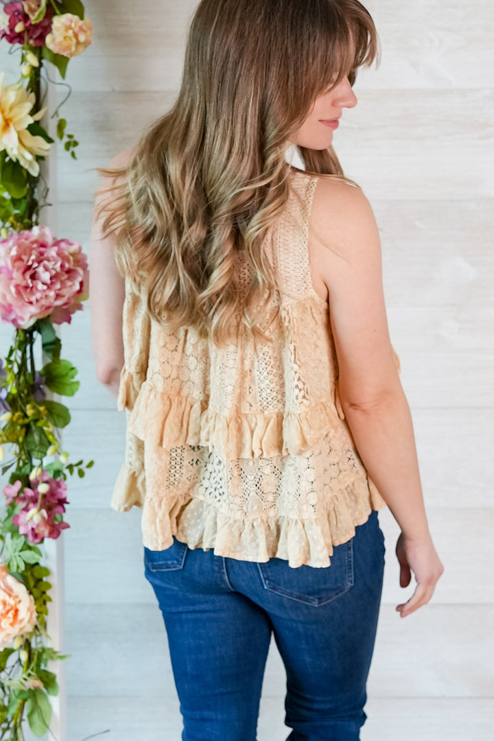 Woman wearing a beige lace tiered tank top and blue jeans with floral decorations on the side.