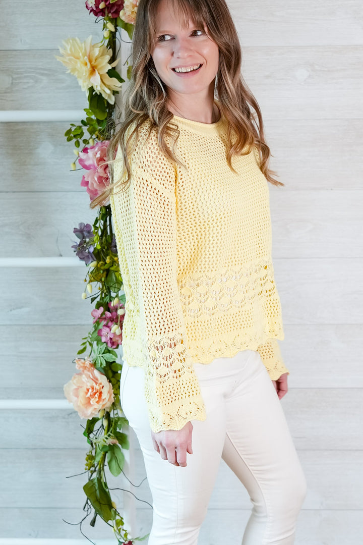 Woman wearing a yellow crochet top standing next to a floral arrangement on a wooden staircase.