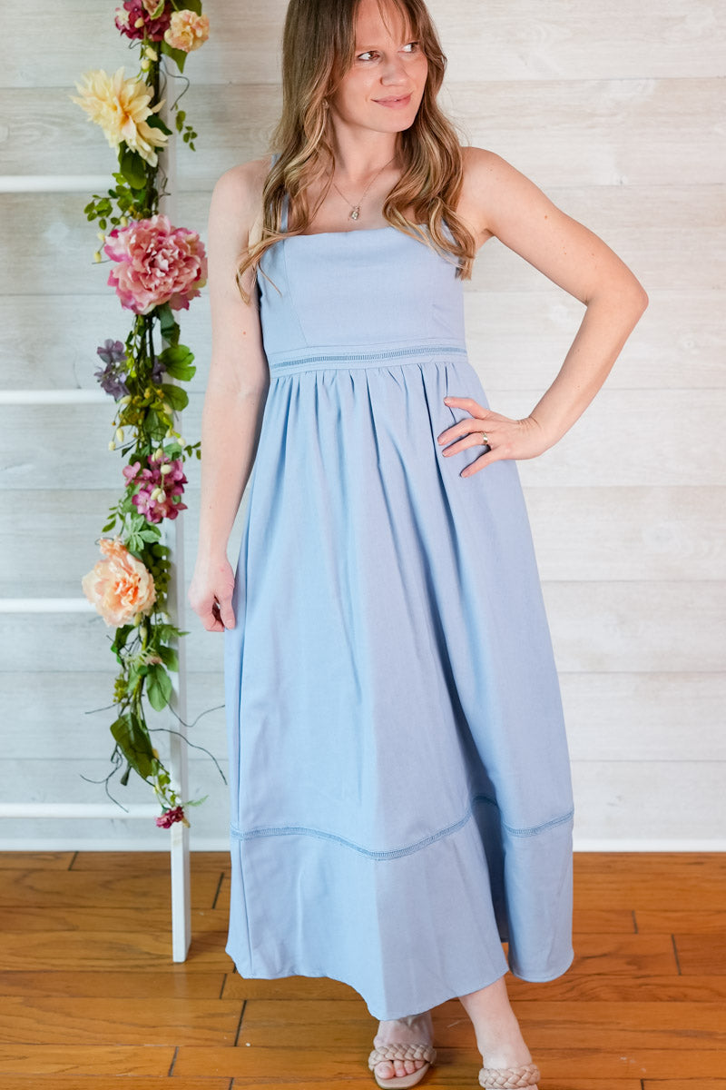 Woman wearing a light blue dress standing next to a floral arrangement indoors.
