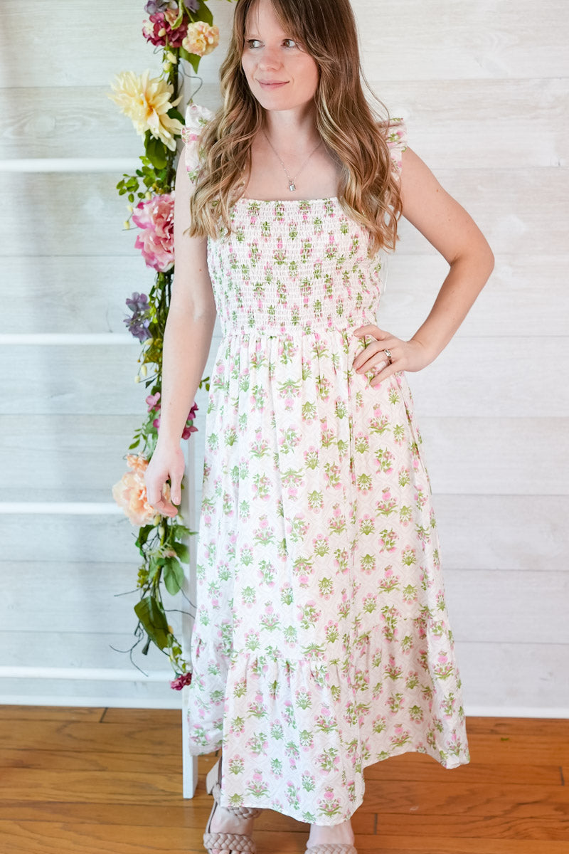 Woman wearing a green and pink smocked floral midi dress standing next to a floral arrangement indoors.