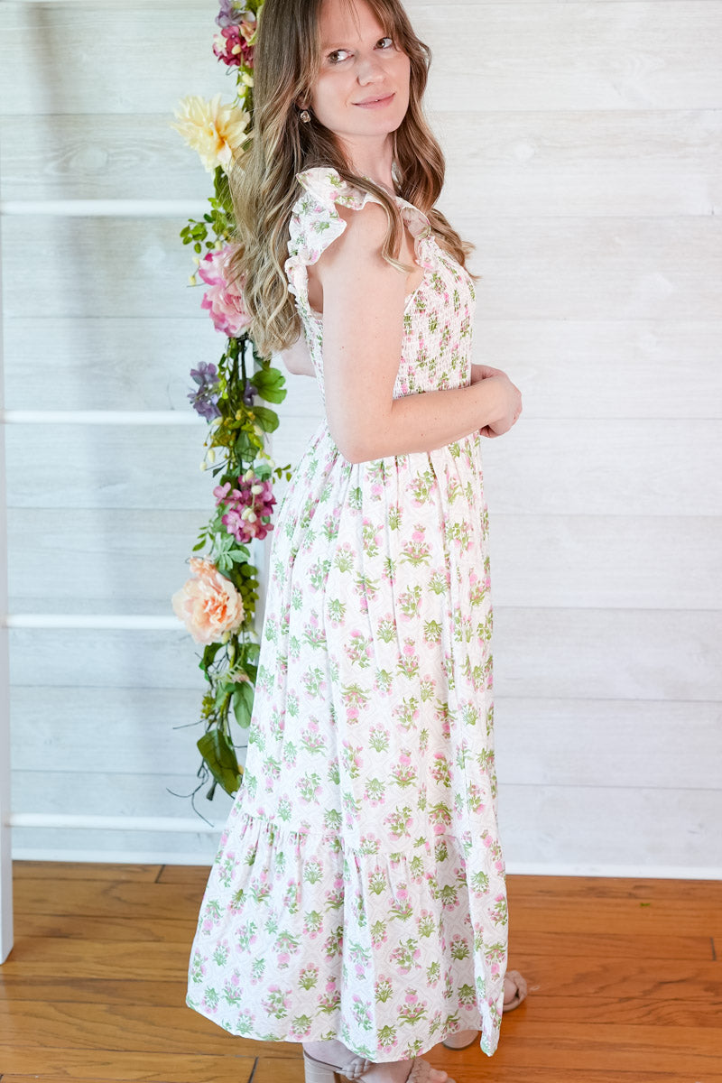 Woman in a pink and green spring floral tiled midi dress standing next to a floral arrangement indoors.