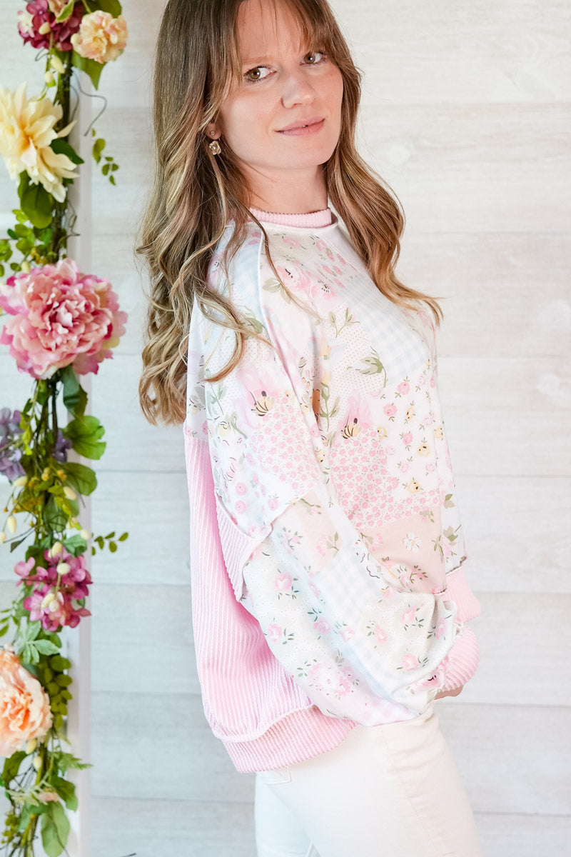 Woman wearing a floral patchwork blouse, standing next to a floral arrangement.