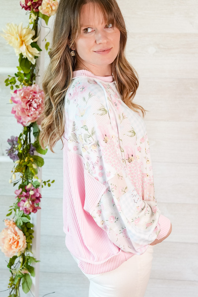 Woman wearing a pink floral patchwork top standing next to a floral arrangement.