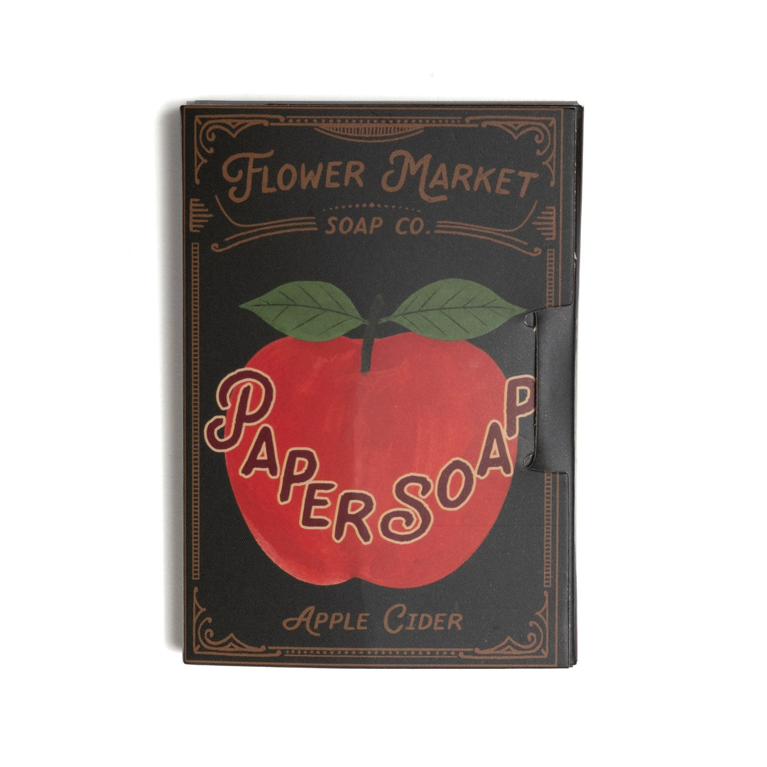 A rectangular package with a vintage-style cover design. The cover is black with a large red apple graphic, green leaves, and tan lettering that reads 'Flower Market Soap Co.