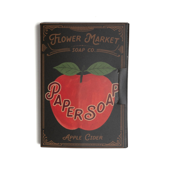 A rectangular package with a vintage-style cover design. The cover is black with a large red apple graphic, green leaves, and tan lettering that reads 'Flower Market Soap Co.